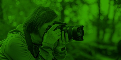 Person fotograferar i skogen med en kamera, bilden har ett grönt filter.
