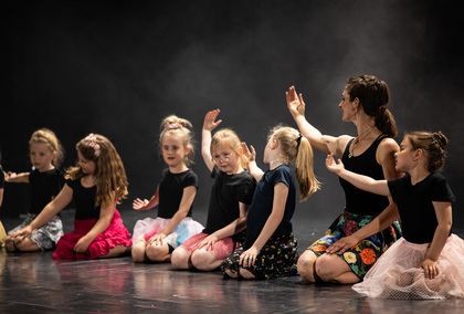 En grupp barn och en vuxen sitter på golvet och dansar tillsammans på en scen.