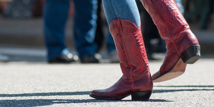 Person i blå jeans och röda cowboyboots dansar utomhus på asfalt.