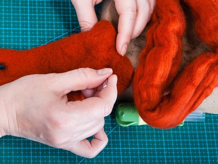 Två händer arbetar med röd ull på en grön skärmatta, troligen för tovning eller hantverk.