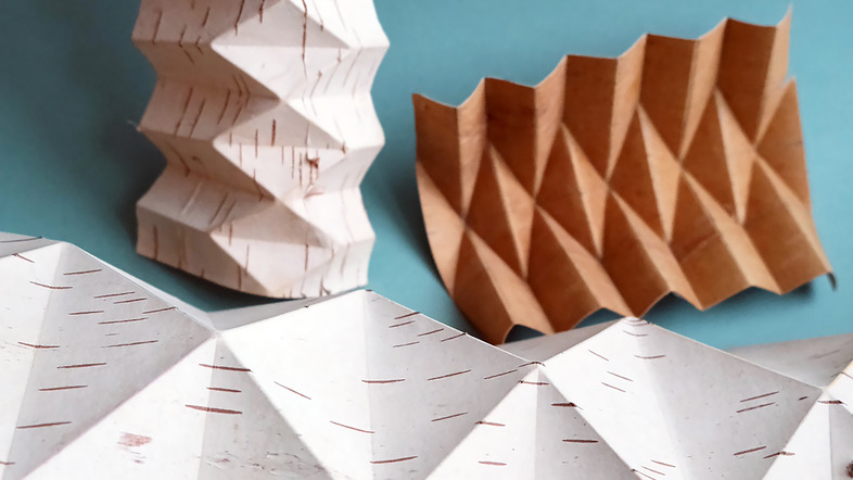 Tre vikta pappersfigurer med geometriska mönster mot en blå bakgrund.