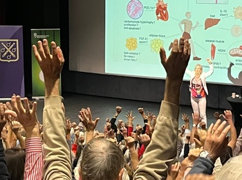 Föreläsning om fysisk aktivitet, hälsa och åldrande. Publik med händerna uppsträckta framför scenen.