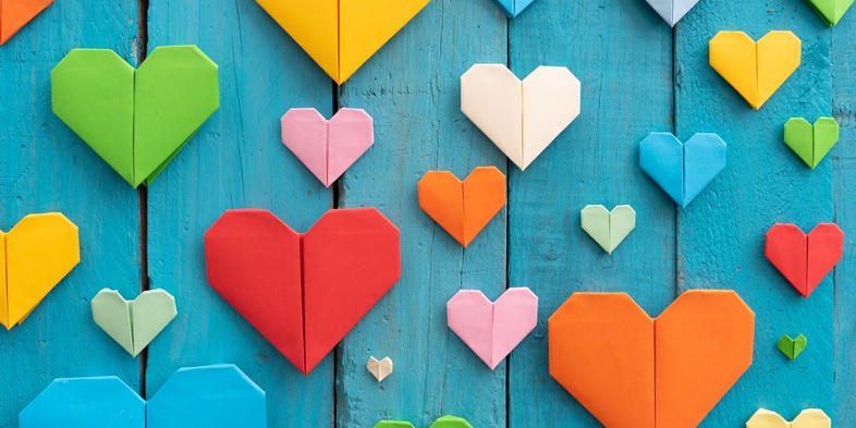 Flera färgglada origamihjärtan i olika storlekar på en blå träbakgrund.