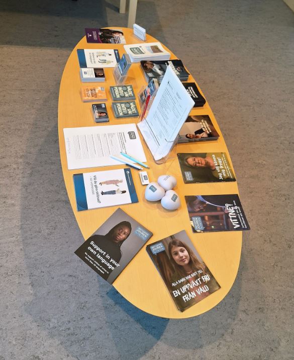 Ett ovalt bord med informationsbroschyrer, pennor och stressbollar i ett väntrum eller kontorsmiljö.