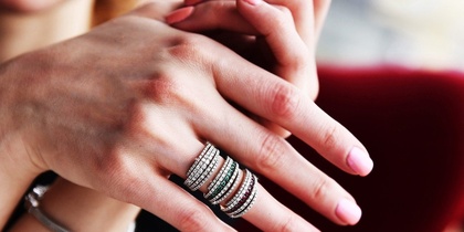 Närbild på händer med flera glittrande ringar och ljusrosa nagellack.
