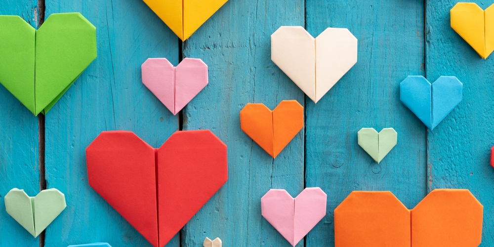 Flera färgglada origamihjärtan i olika storlekar på en blå träbakgrund.
