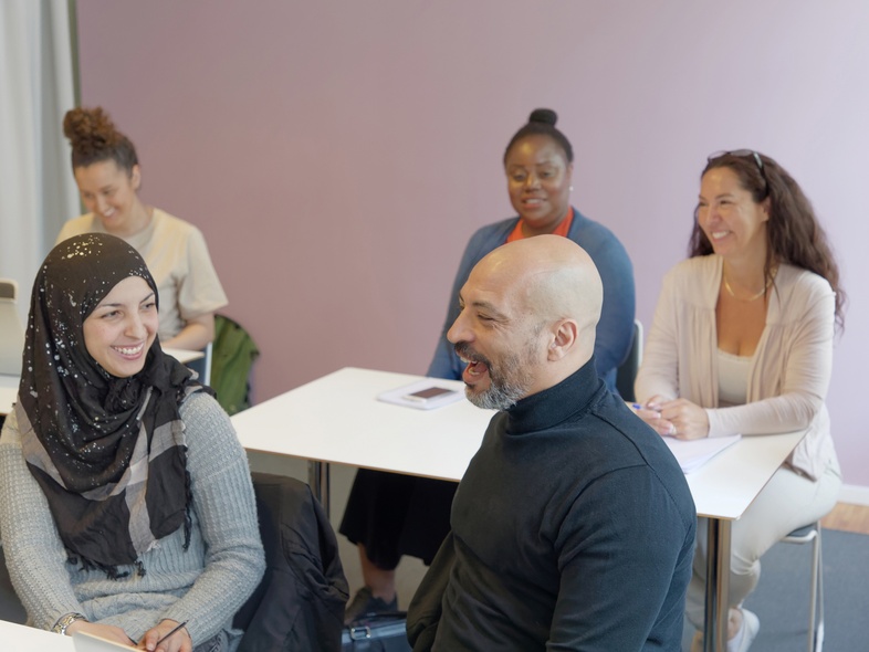 Fem personer sitter i ett klassrum och samtalar, alla ser glada ut.