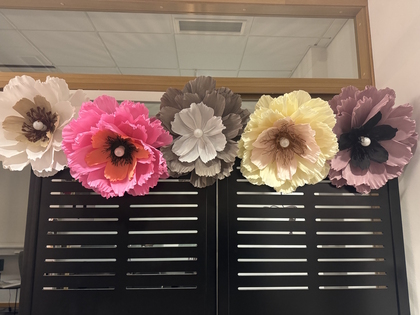 Fem stora, färgglada pappersblommor sitter fast på en svart skärm framför en spegel.