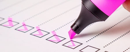 En hand markerar rutor på en checklista med en rosa överstrykningspenna.