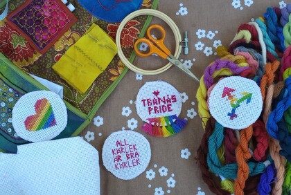 Broderimaterial och färgglada broderier med regnbågsmotiv och text på ett bord.
