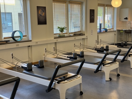 Ett ljust pilatesrum med flera reformermaskiner, stora fönster och träningsredskap på fönsterbrädorna.