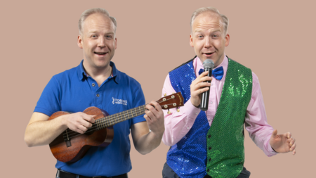 Två män, en i blå pikétröja med ukulele och en i färgglad väst med mikrofon, står bredvid varandra mot beige bakgrund.