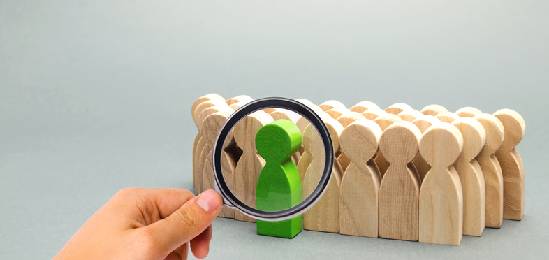 En mängd träfigurer granskas av en hand med förstoringsglas.