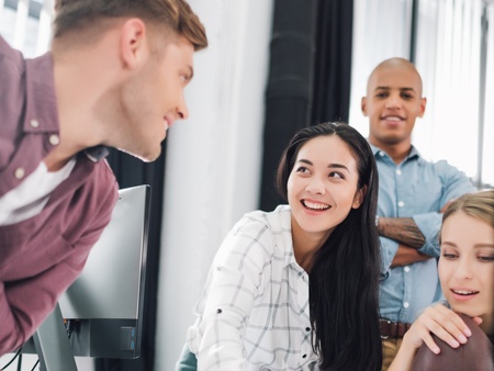 Fyra unga vuxna samarbetar och diskuterar vid ett skrivbord på ett modernt kontor.