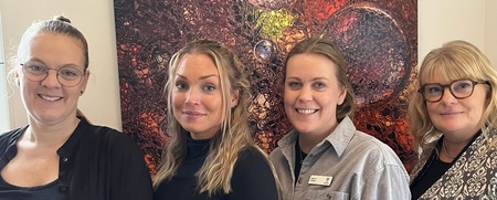 Fyra kvinnor står bredvid varandra framför en färgstark tavla med bubblor och abstrakta mönster.