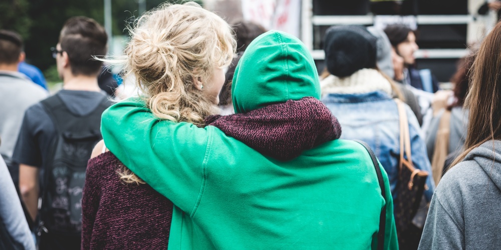 Två personer står tätt tillsammans i en folkmassa, en med grön hoodie har armen om den andra.