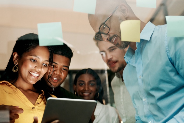 En grupp unga vuxna samarbetar och tittar på en surfplatta i ett modernt kontorsutrymme.