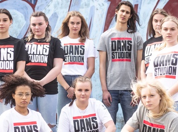 En grupp unga personer poserar framför en graffitivägg, alla bär t-shirts med texten 'Dansstudion'.