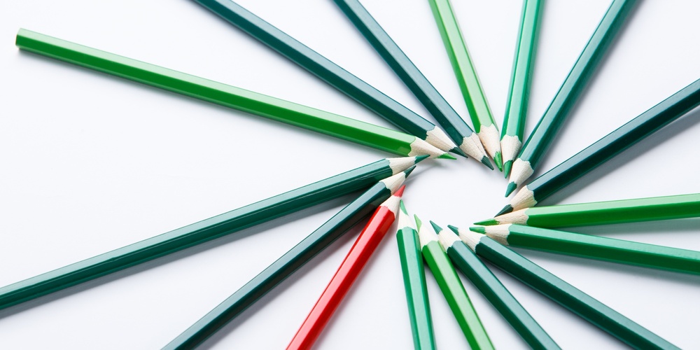 Flera gröna och en röd färgpenna ligger i en cirkel på ett vitt underlag.