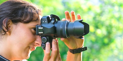 Två kvinnor fotograferar utomhus i grönskande miljö, med en tredje person i bakgrunden.
