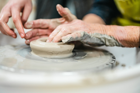 Två par händer formar lera på en drejskiva under en keramikkurs.