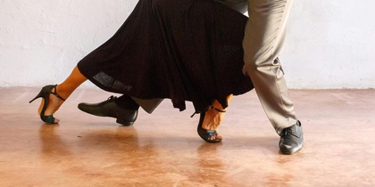 Ett par dansar tango i en elegant pose mot en ljus vägg.