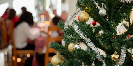 Närbild på en dekorerad julgran med kulor och glitter, suddig familj i bakgrunden vid matbord.