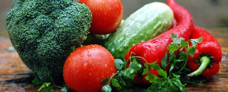 En samling färska grönsaker, inklusive broccoli, tomater, gurka, paprika och persilja på en träyta.
