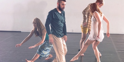 Fyra personer dansar barfota på ett svart golv i en ljus dansstudio.