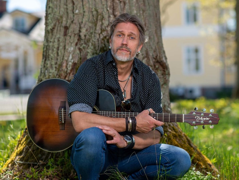 Man som sitter lutad mot ett träd med en gitarr i handen