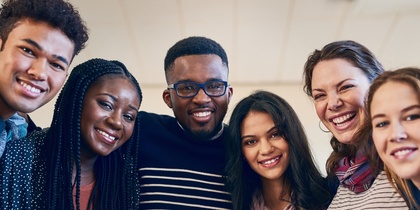 Sex unga vuxna står tätt tillsammans och ler mot kameran i ett ljust rum.