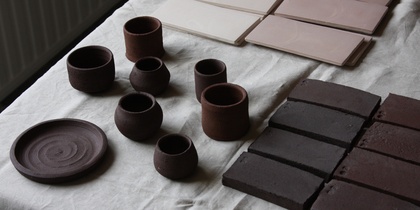 Flera små keramikskålar, en tallrik och rektangulära plattor i olika färger ligger på en vit duk.