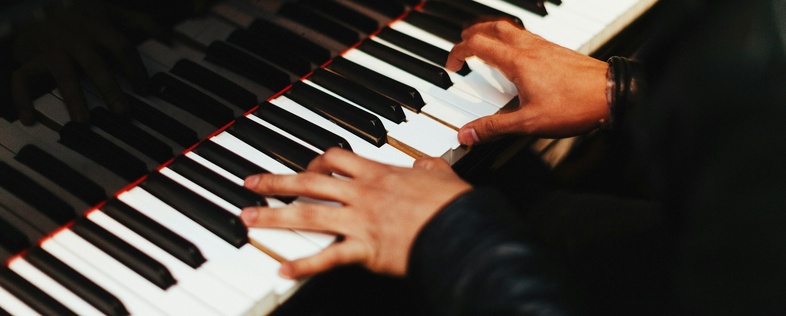 Närbild på händer som spelar på ett piano, fokus på tangenter och fingrar.