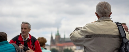 Flera personer står utomhus, några fotograferar, med en stadssilhuett och slott i bakgrunden.