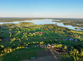 Landskapsvy över gröna fält, gårdar och sjöar under klarblå himmel.