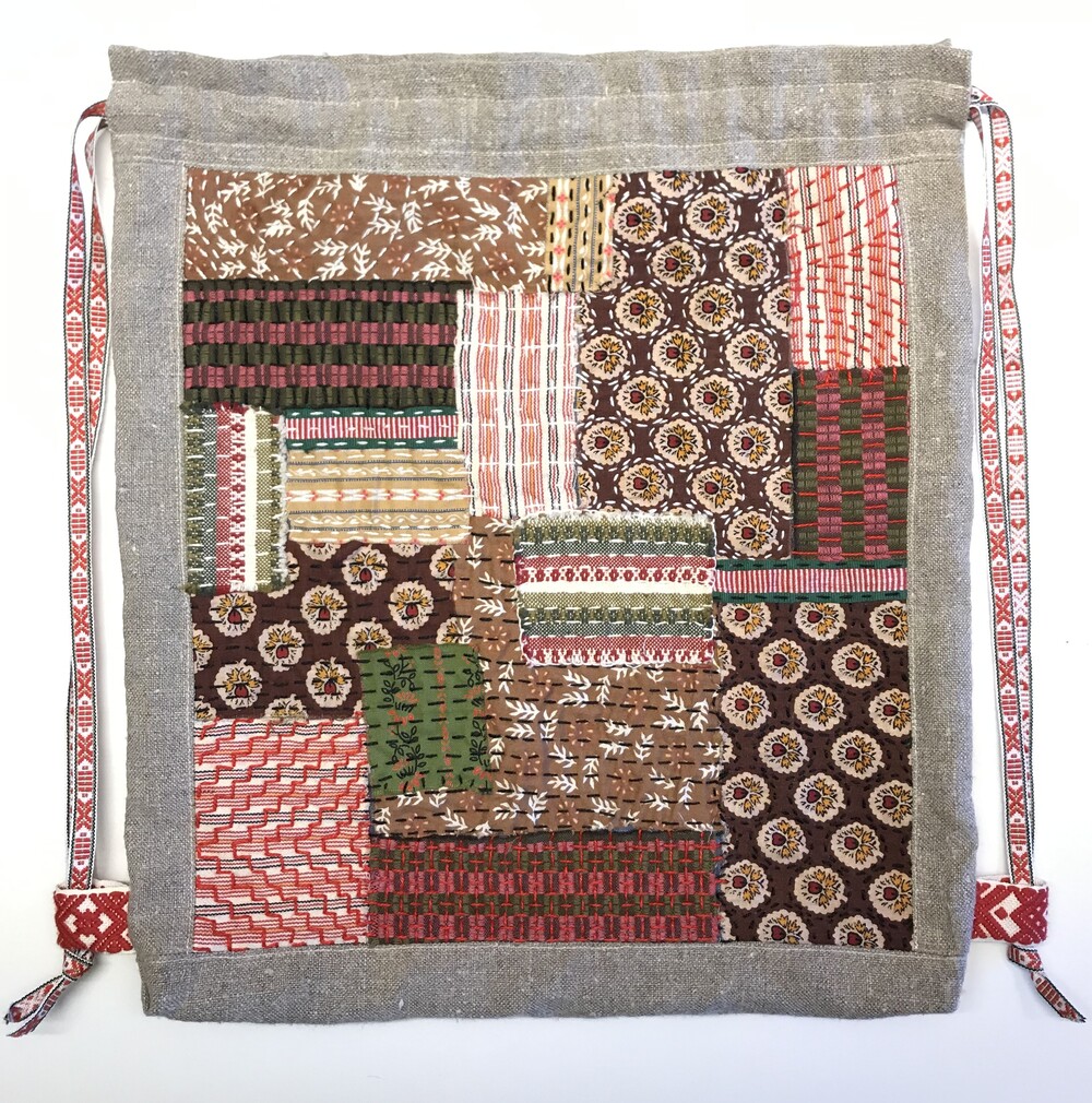Patchworkpåse i bruna, röda och gröna tyger med mönster, kantad med grått tyg och röda band.