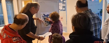 En grupp människor samlas runt en whiteboard i ett ljust rum för en gemensam diskussion.