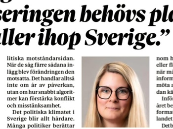 Flera personer skriver tillsammans på ett stort papper vid ett bord, fokus på händer och pennor.