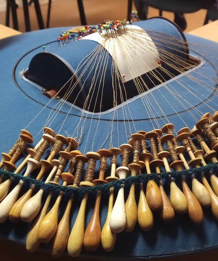 Närbild av en spetsknypplingsdyna med många trådar och träspolar, används för att skapa spetsmönster.