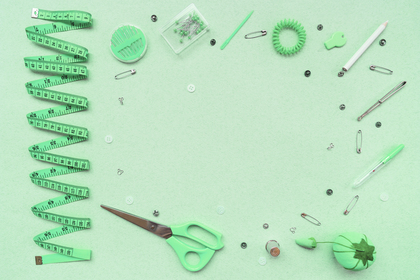 Sytillbehör som sax, måttband, nålar och knappar ligger utspridda på ett grönt underlag.