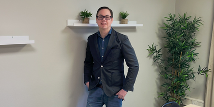 En person står vid väggen i ett mötesrum med bord, stolar, växter och hyllor med krukväxter.