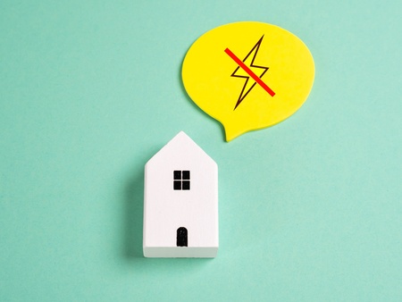 En vit modell av ett hus med en pratbubbla som visar en överkryssad blixt, på grön bakgrund.