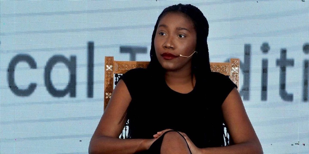 Person sitter på en stol med armarna vilande och benen i kors framför en stor textskärm.