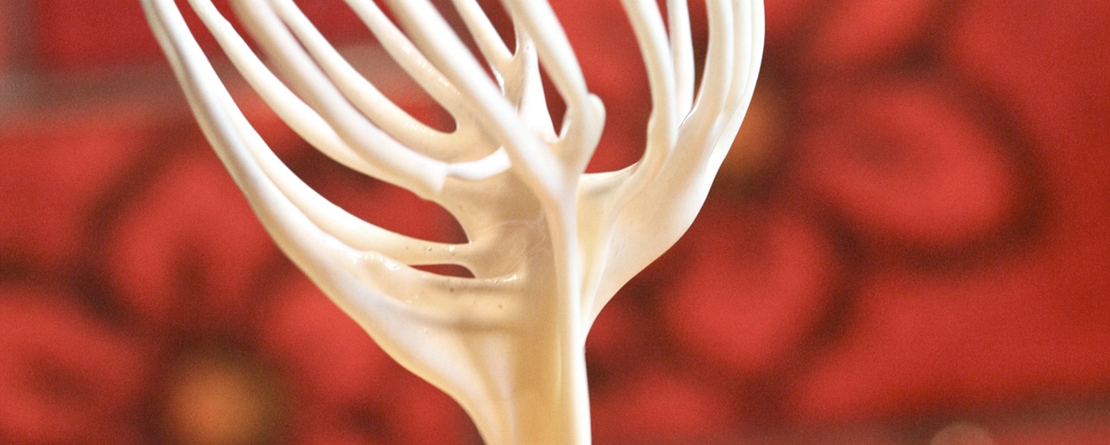 En visp med smet droppar ner i en gul skål, med röd bakgrund med blommönster.