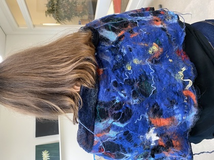 Person med axellångt hår sedd bakifrån, bär en färgglad blå sjal i ett ljust rum.