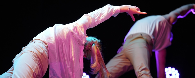 Två personer utför en modern dansrörelse på scen med färgglad belysning.