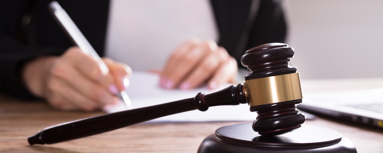 En domarklubba ligger på ett skrivbord medan en person skriver på papper i bakgrunden.