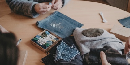 Tre personer sitter runt ett bord och arbetar med tygbitar och broderimaterial.