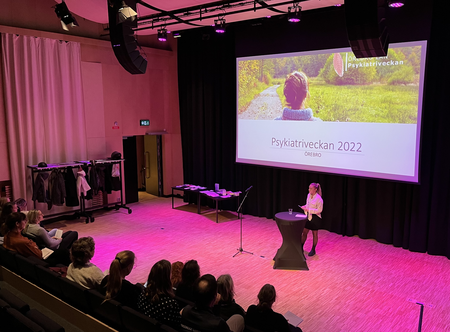 En kvinna står på scen och talar inför en sittande publik under Psykiatriveckan 2022.
