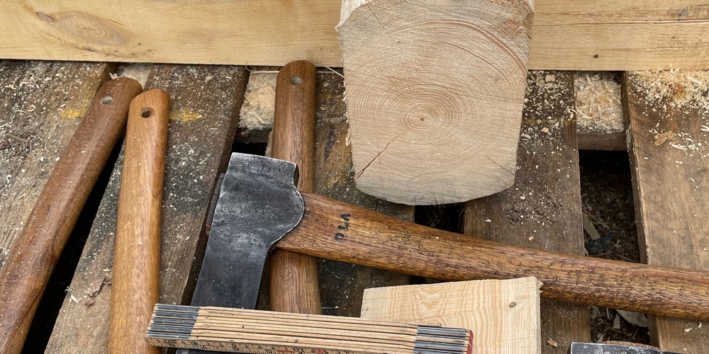 Flera yxor, träbitar och verktyg ligger på en träpall utomhus, redo för träbearbetning.